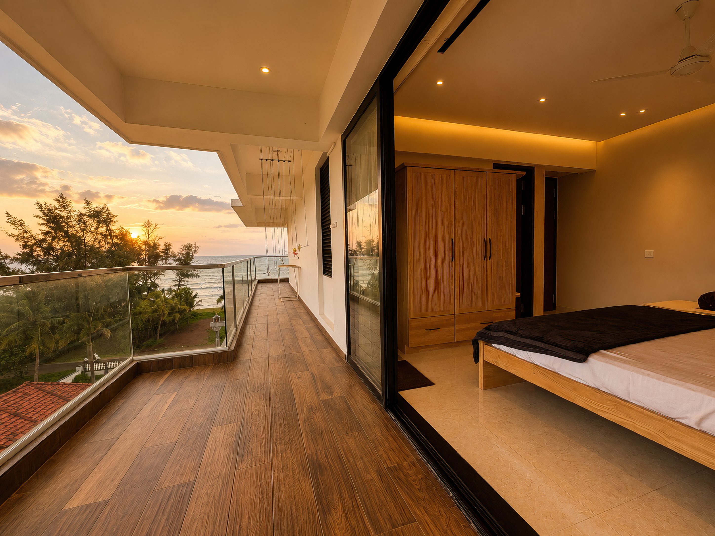 Wooden balcony off a bedroom, looking over the palms to the sea at sunset